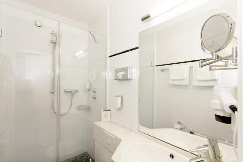 ein weißes Bad mit einer Dusche und einem Waschbecken in der Unterkunft Hotel Scala Frankfurt City Centre in Frankfurt am Main