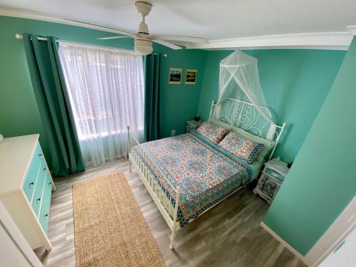 Dormitorio verde con cama y ventana en Gaia Vida River Cottage, en Lowood