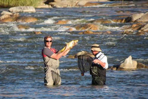two men standing in a river holding a fishing net at Tutwa Desert Lodge in Augrabies