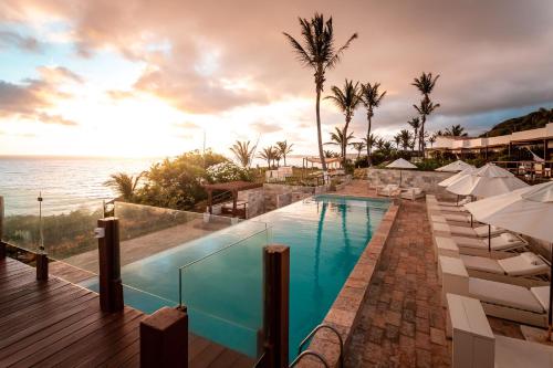 uma piscina num resort com guarda-sóis e o oceano em Pipa Privilege Suítes em Pipa