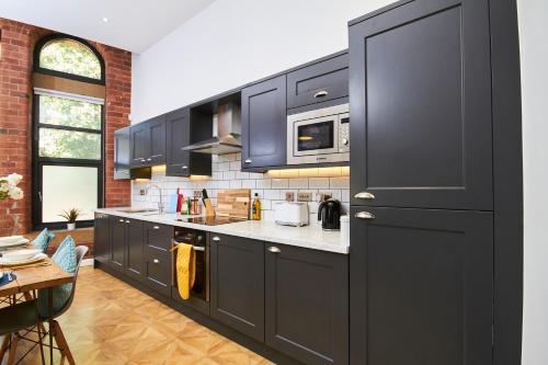 a kitchen with black cabinets and a brick wall at 2Bed NYC Style Apartment in Central Leeds in Leeds