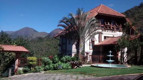 a house with a palm tree and a fountain in front of it at Hotel Dominguez Master in Nova Friburgo