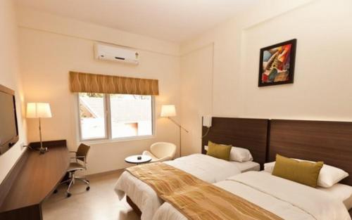 a bedroom with two beds and a desk and a television at Mallige Residency in Hassan