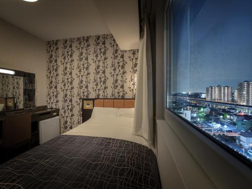 um quarto com uma cama e uma janela com uma cidade em APA Hotel Ibaraki Koga Ekimae em Koga