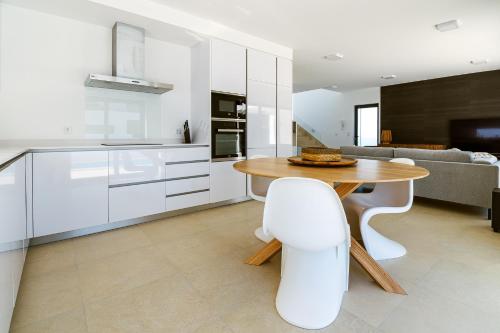 a white kitchen with a wooden table and white chairs at Villa Chaves in Óbidos