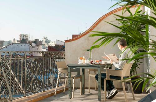 a man sitting at a table with a laptop on a balcony at Eric Vökel Boutique Apartments - Madrid Suites in Madrid