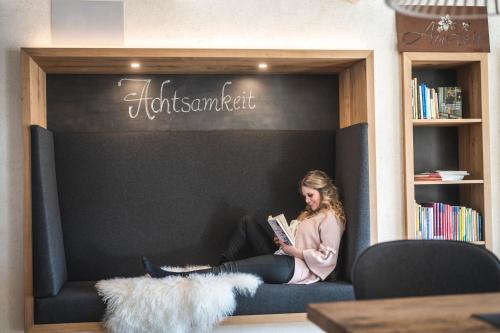 a woman sitting on a couch reading a book at Hotel Natur-Landhaus Krone in Maierhöfen