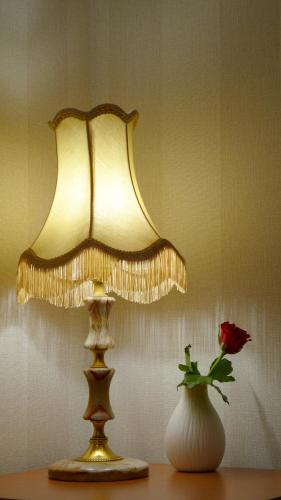 a table with a lamp and a vase with a rose at Wrzos & Belvedere in Kudowa-Zdrój