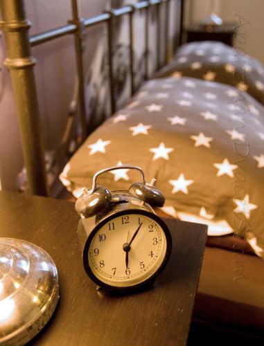 a clock sitting on a table next to a bed at Apartman DvacetSedm in Lipno nad Vltavou
