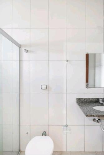 a white tiled bathroom with a toilet and a sink at Nosso Hotel in Campo Grande