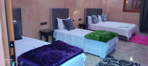 a room with three beds with purple and green sheets at Hôtel Ajil Cascades D'ouzoud in Ouzoud