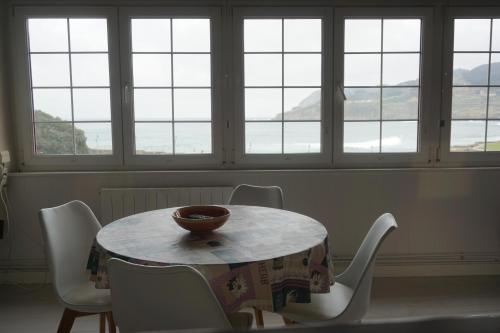 a table with chairs and a bowl on it in a room with windows at ATICO TORRONTERO in Mundaka