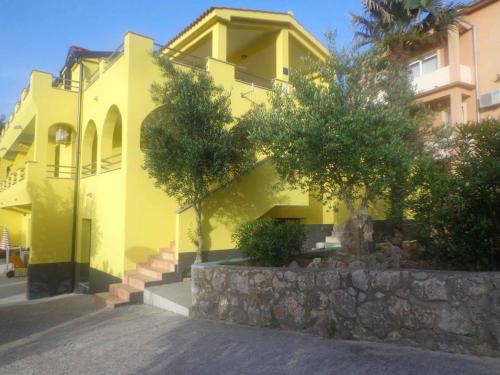 a yellow house with stairs and trees in front of it at Apartment Vrbnik 8 in Vrbnik