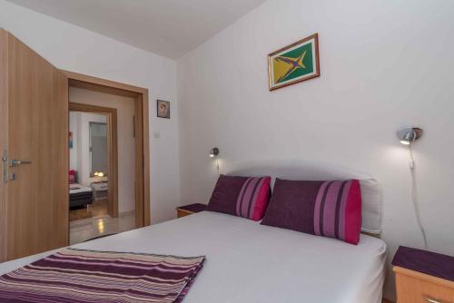 a bedroom with a white bed with purple pillows at Apartment Okrug Gornji, Ciovo 2 in Trogir