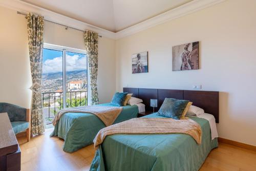 two beds in a room with a window at Luxury two bedroom Palheiro Village by HR Madeira in São Gonçalo