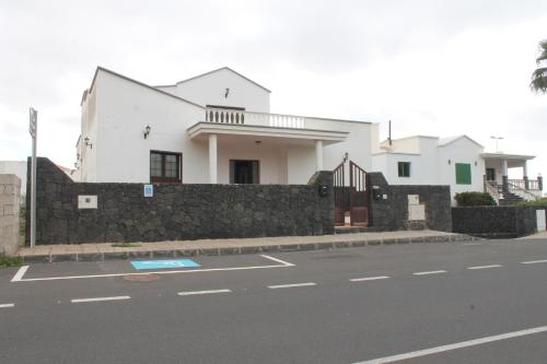 a white house behind a stone wall next to a street at El sueño - Le rêve in San Bartolomé