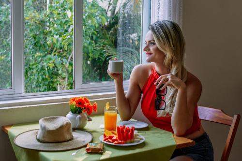 a woman sitting at a table with a cup of coffee at Pousada Tortugas in Guarujá