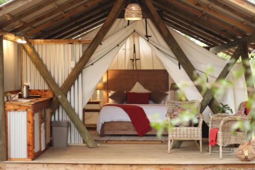 een slaapkamer in een tent met een bed en stoelen bij Heritage Glamping, Woodlands tent in Wilderness