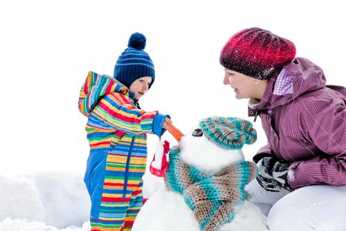 two children playing with a snowman in the snow at Hotel Zürserhof in Zürs am Arlberg