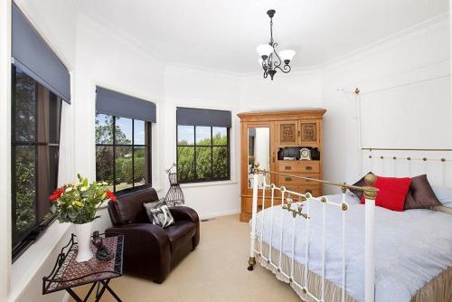 a bedroom with a bed and a chair and windows at Stately Bowral Designer Home in Bowral