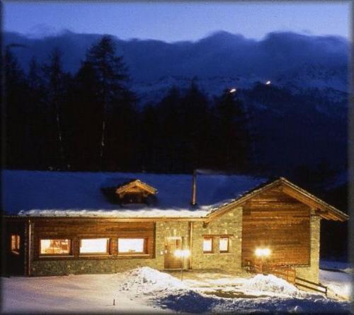 a log house with snow on the roof at night at Hotel Les Granges in La Thuile