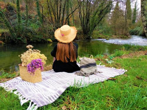 a woman sitting on a picnic blanket next to a river at Terra Rosa Country House & Vineyards in Ponte de Lima