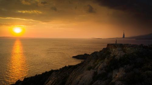 a person standing on a cliff with the sun setting at Niriides in Porto Koufo