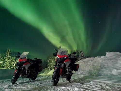 two motorcycles parked in the snow under the northern lights at Villa Björklund - Lakeview Apartment in Arjeplog