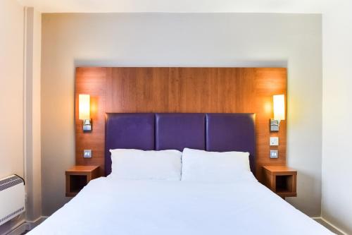 a bedroom with a large bed with a blue headboard at Tyger Inn Derby in Derby
