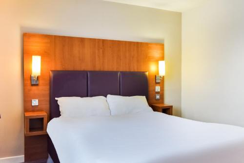 a bedroom with a large white bed with a wooden headboard at Tyger Inn Derby in Derby