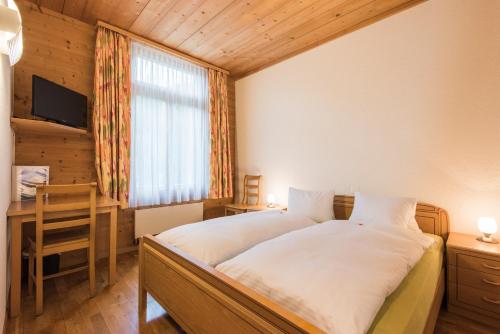 a bedroom with a bed and a desk and a window at Hotel Alpenrose beim Ballenberg in Brienz
