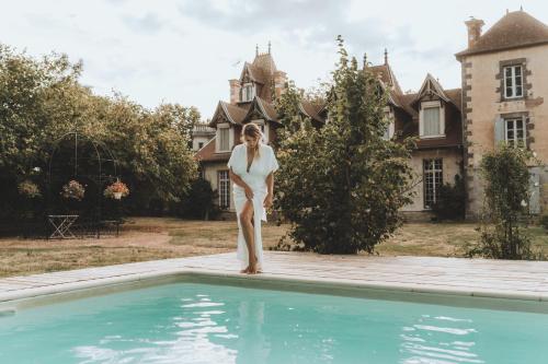 Eine Frau steht neben einem Pool vor einem Haus. in der Unterkunft Château Du Guérinet in Saint-Priest-Bramefant