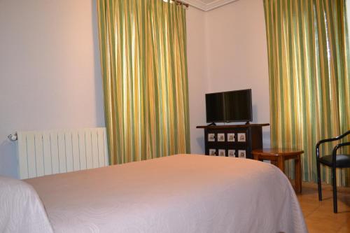 a bedroom with a bed and a tv and curtains at Hostal Aribel Longinos in Cercedilla