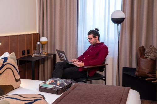 a man sitting in a chair with a laptop in a hotel room at Hôtel du Port in Nogent-sur-Marne