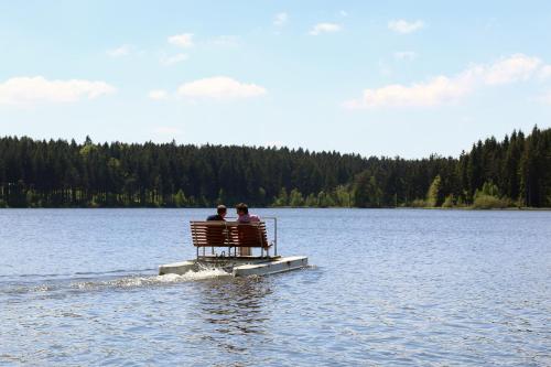 two people sitting on a bench on a dock in a lake at Hotel Medlov Depandance in Fryšava