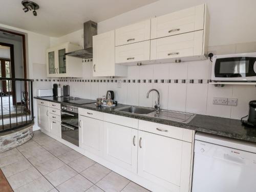 a kitchen with white cabinets and a sink and a microwave at Caecrwn in Brecon