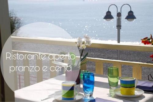 a table with glasses and flowers on a balcony with the ocean at Hotel Piccolo Paradiso in Bordighera