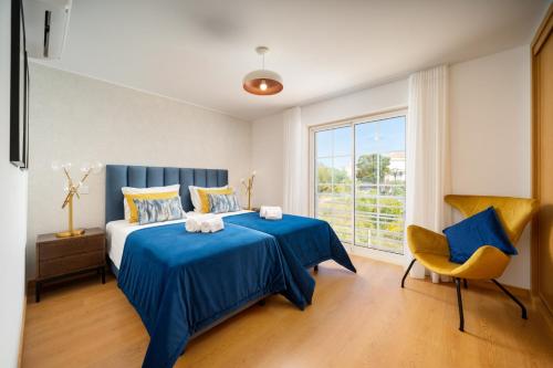 a bedroom with a blue bed and a yellow chair at Fresh & Breezy Tavira Apartment in Cabanas de Tavira