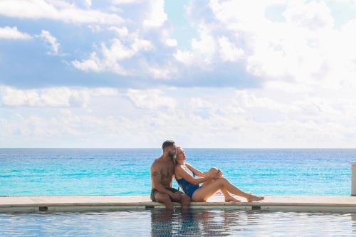 a man and woman sitting in a swimming pool overlooking the ocean at Sandos Cancun All Inclusive in Cancún