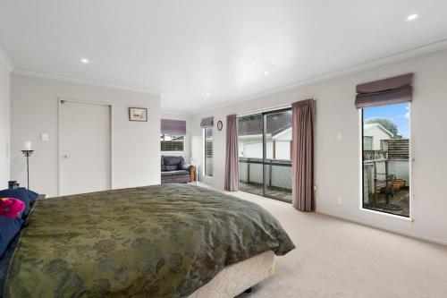 1 dormitorio con 1 cama grande y ventanas grandes en Hit The Beach - Waitarere Beach Holiday Home, en Waitarere