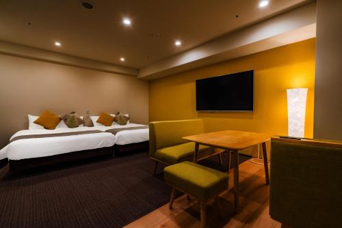 a hotel room with two beds and a table and a television at Randor Hotel Sapporo Suites in Sapporo
