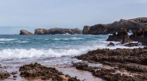 a beach with rocks and the ocean with waves at Posada La Morena in Soto de la Marina