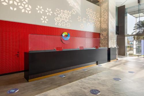 a lobby with a red wall and a counter at Ramada Encore by Wyndham Muscat Al-Ghubra in Muscat