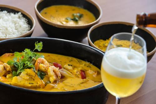 a bowl of chicken curry and a glass of beer at Vidam Hotel Aracaju - Transamerica Collection in Aracaju