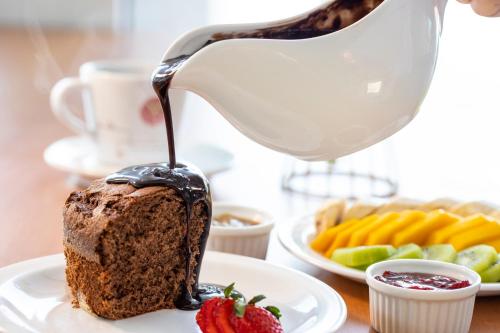 a person pouring chocolate sauce onto a piece of cake at Vidam Hotel Aracaju - Transamerica Collection in Aracaju