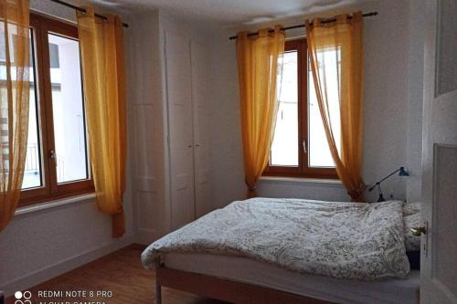 a bedroom with a bed and two windows with orange curtains at NOUVEAU! Dans résidence Alexandra House in Leysin
