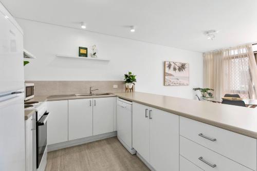 a white kitchen with white cabinets and a sink at The Noosa Apartments in Noosa Heads