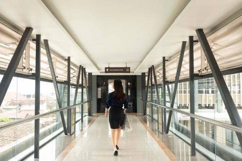 a woman walking down a walkway in a building at GRAMM HOTEL by Ambarrukmo Yogyakarta in Yogyakarta