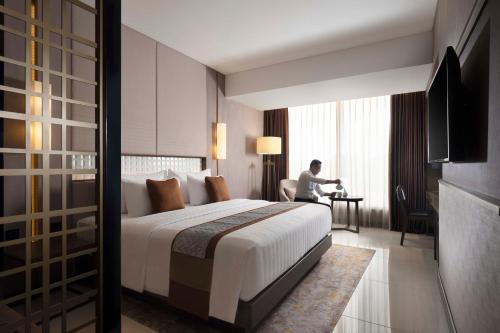 a hotel room with a bed and a man sitting at a desk at GRAMM HOTEL by Ambarrukmo Yogyakarta in Yogyakarta