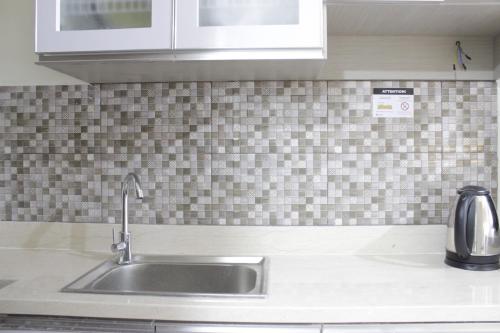 a kitchen with a sink and a tiled wall at Stylish Studio Apartment at Harvard Jatinangor near ITB By Travelio in Sayang